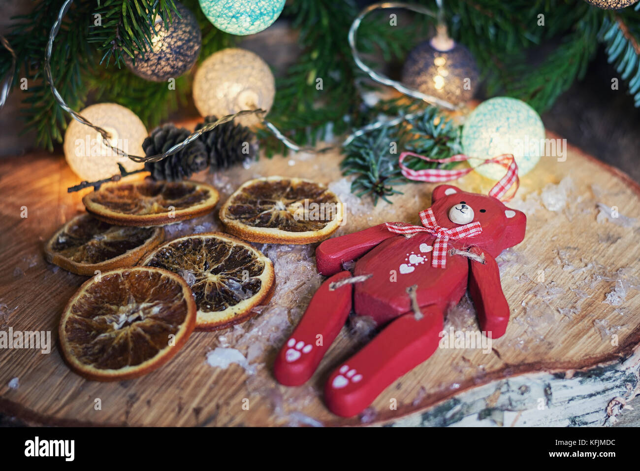 Oso de madera roja tumbado sobre un disco de madera de abedul delante de una sucursal de navidad decorado con bolas de Navidad iluminado Foto de stock