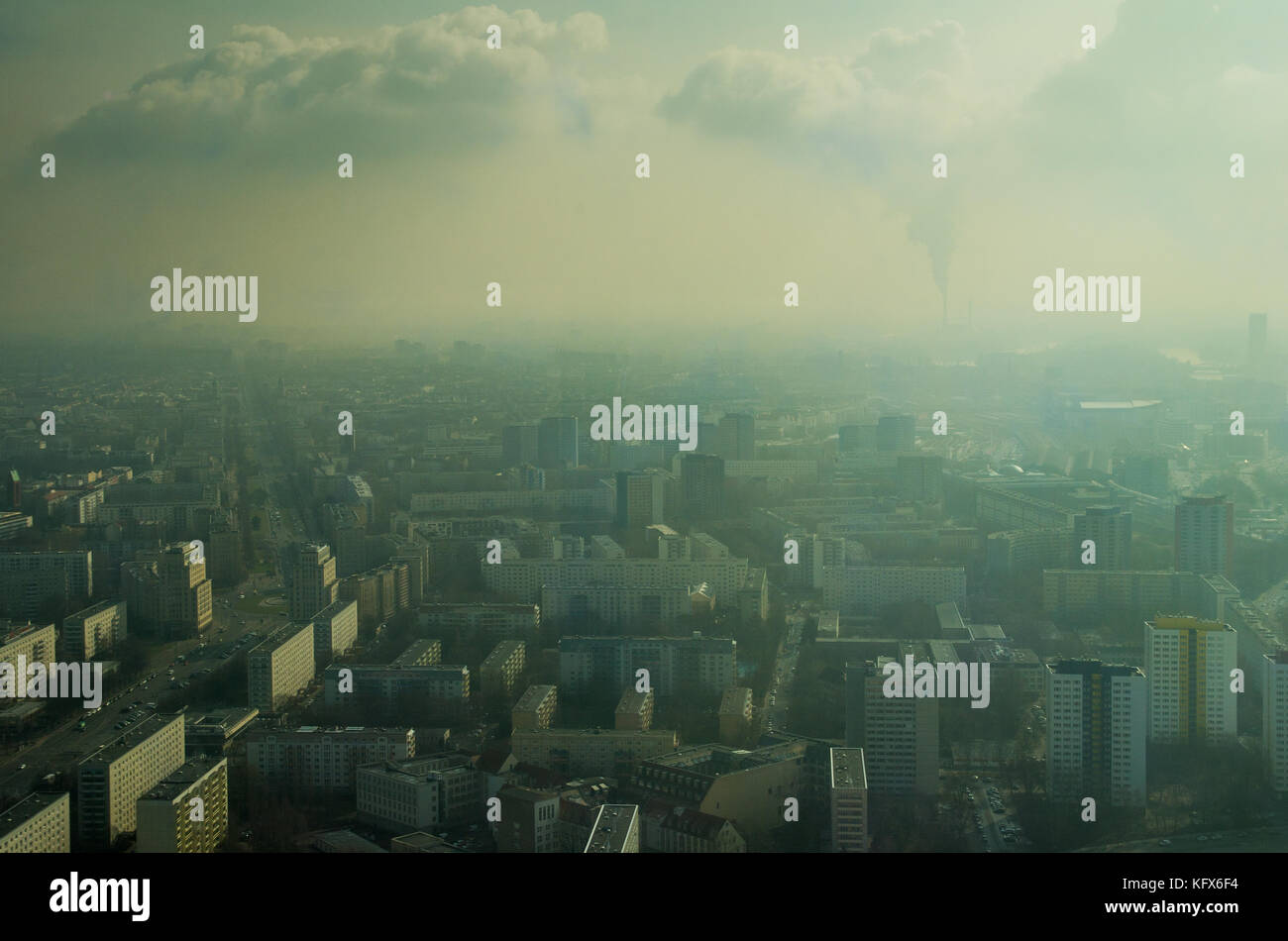 Una vista de Berlín llena de neblina desde la torre de televisión con edificios de varios pisos y una chimenea de fumar en la distancia. Parece una ciudad llena de humo. Foto de stock