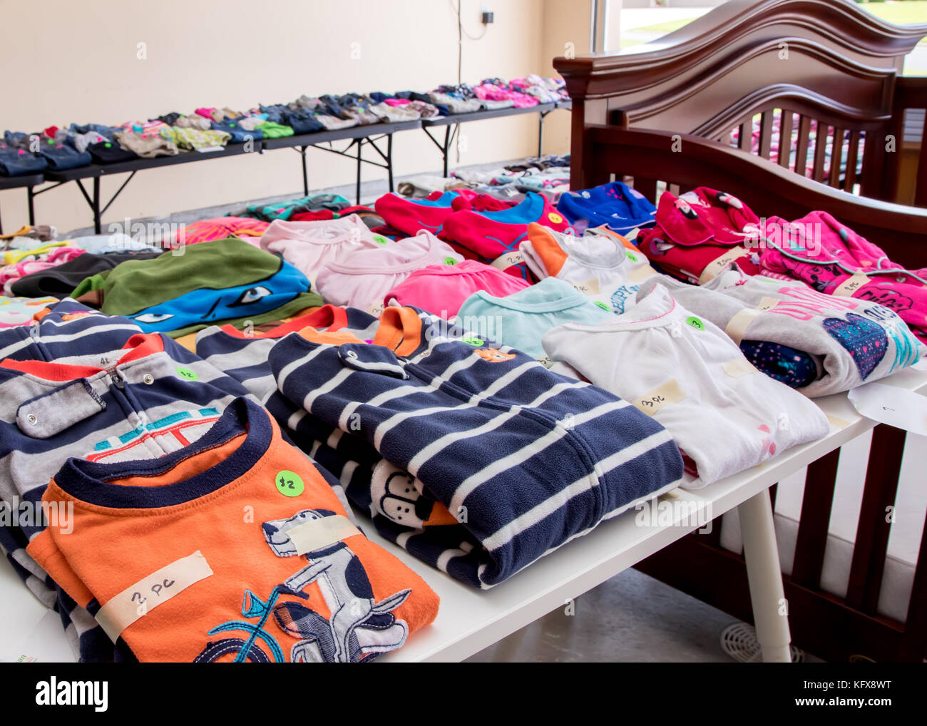 Tablas de prendas de vestir y productos para bebés dispuestos en una venta de garaje suburbano Foto de stock