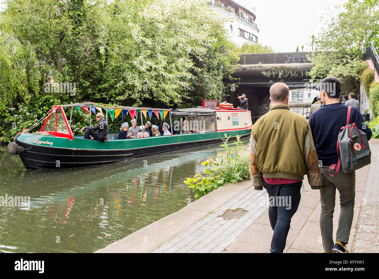 Narrowboat o barcaza pasando sobre el Regents Canal con gente caminando en el camino de sirga canalside cerca de la ciudad de Camden, Londres, Inglaterra, Reino Unido. Foto de stock
