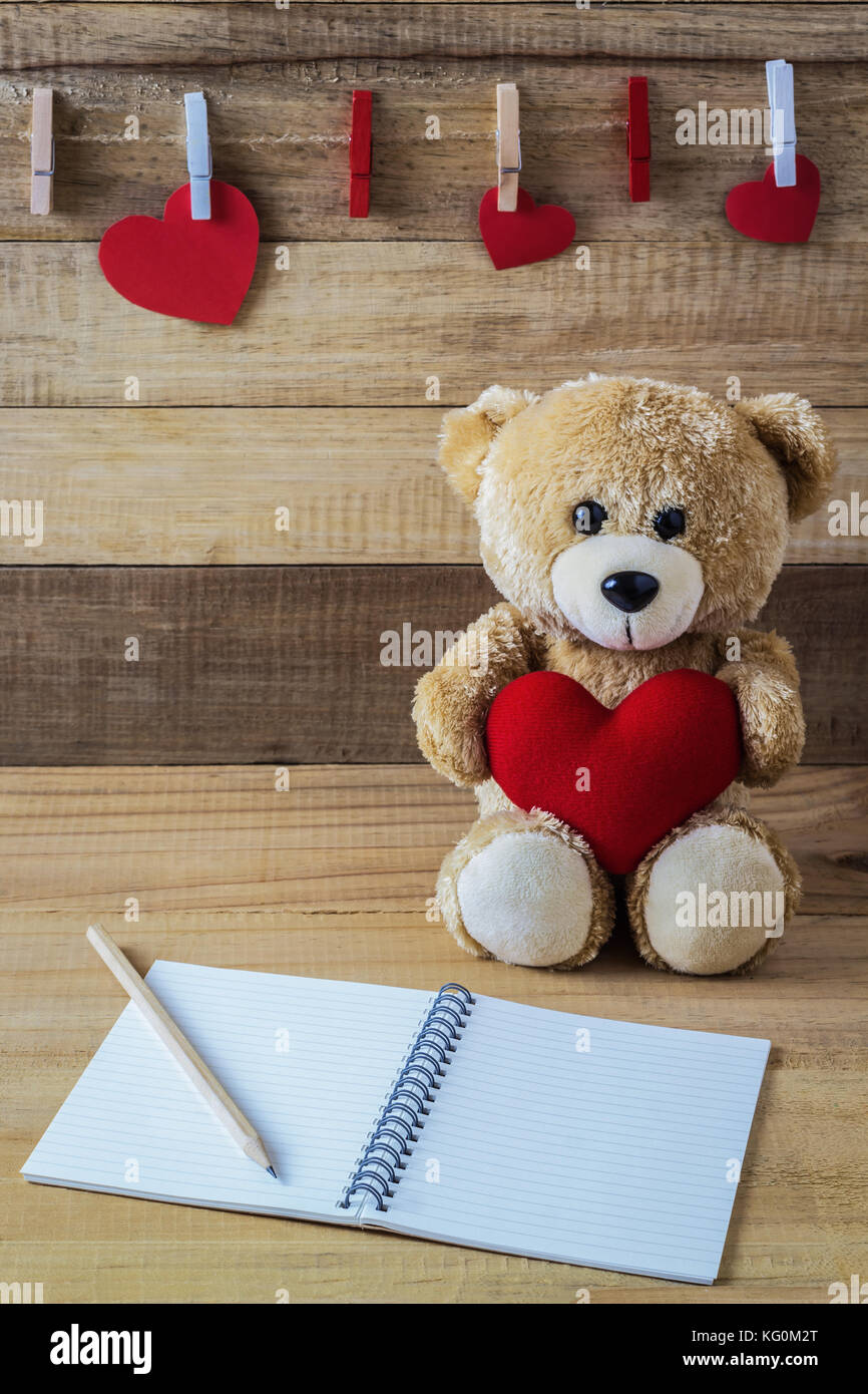 Una foto de oso de peluche sosteniendo una almohada con forma de corazón  sobre la mesa de madera con papel de bloc de notas Fotografía de stock -  Alamy