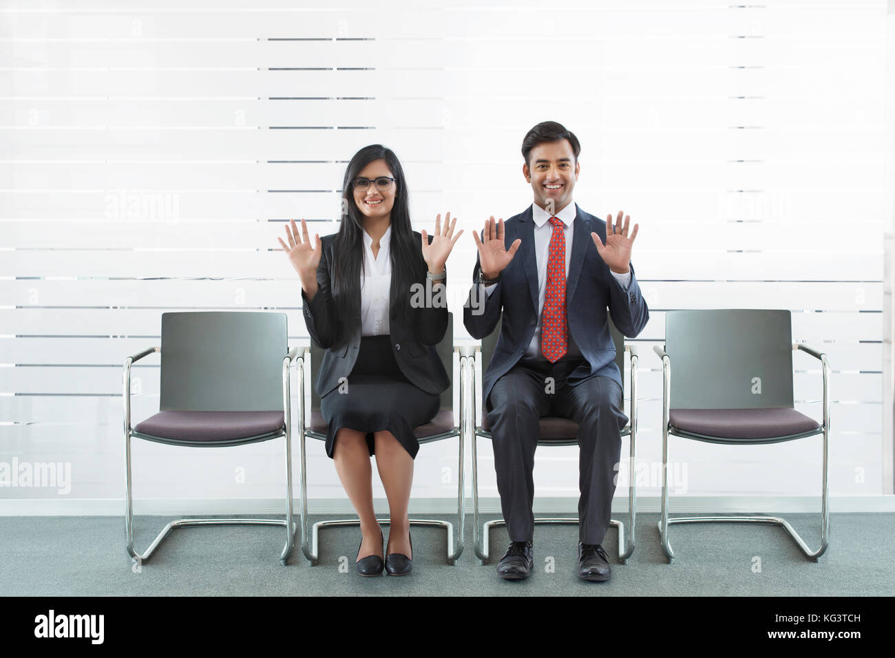 Retrato del empresario sonriente y empresaria mostrando las manos sentado en silla de oficina Foto de stock