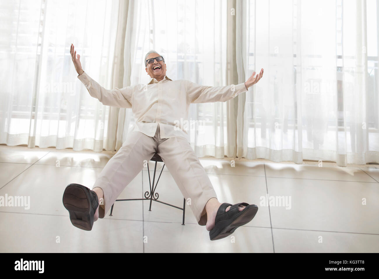 Senior sonriente hombre sentado en una silla con brazos y piernas extendidas Foto de stock