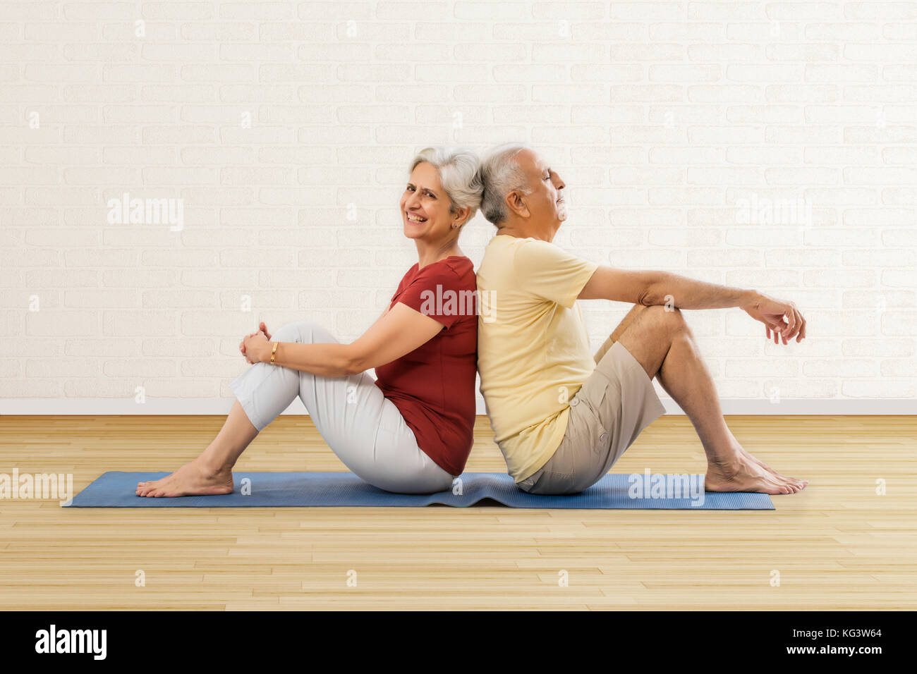 Las parejas ancianas sentados espalda con espalda en la estera del yoga Foto de stock
