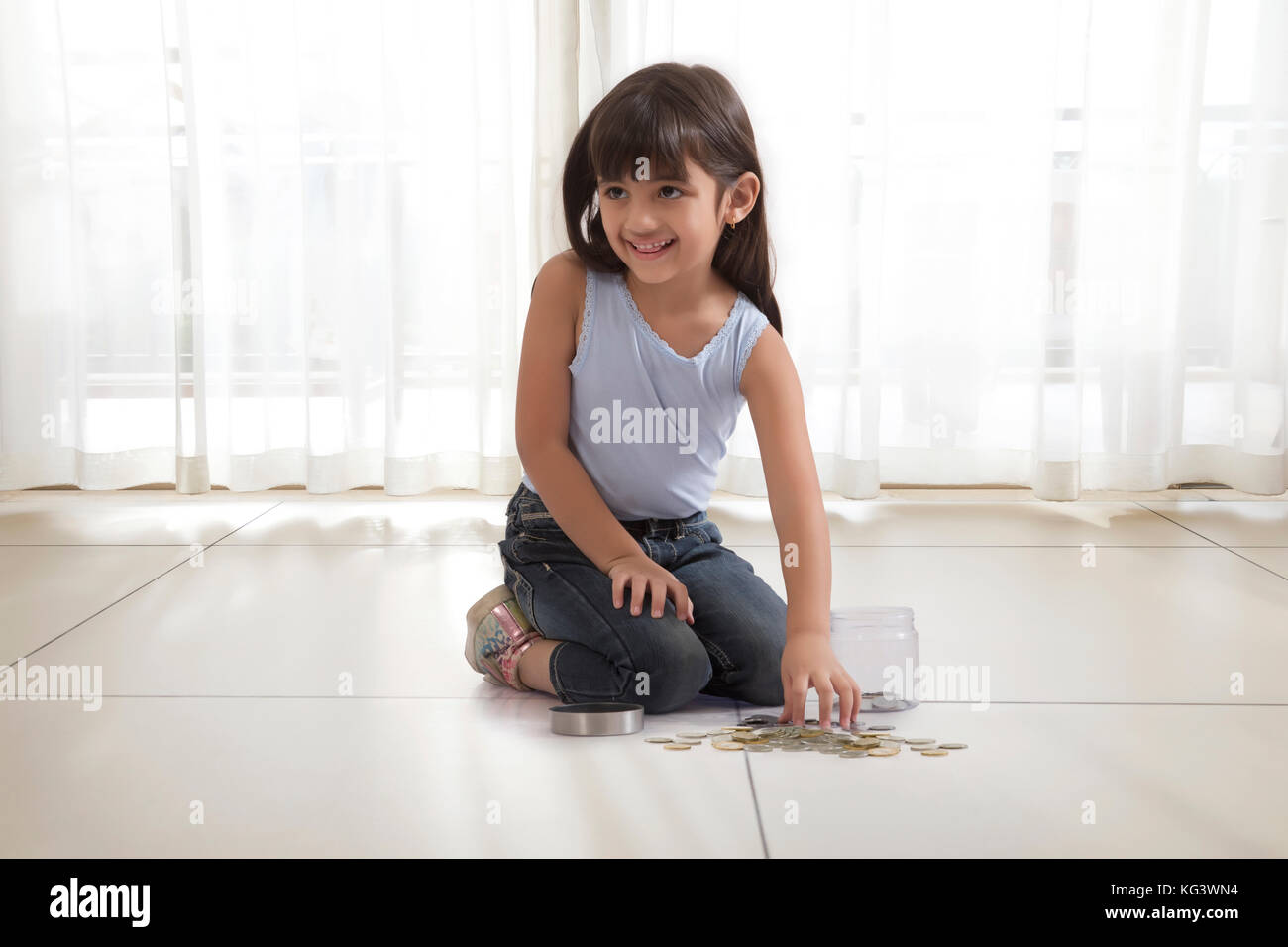 Niña con caja de monedas y monedas en el piso Foto de stock