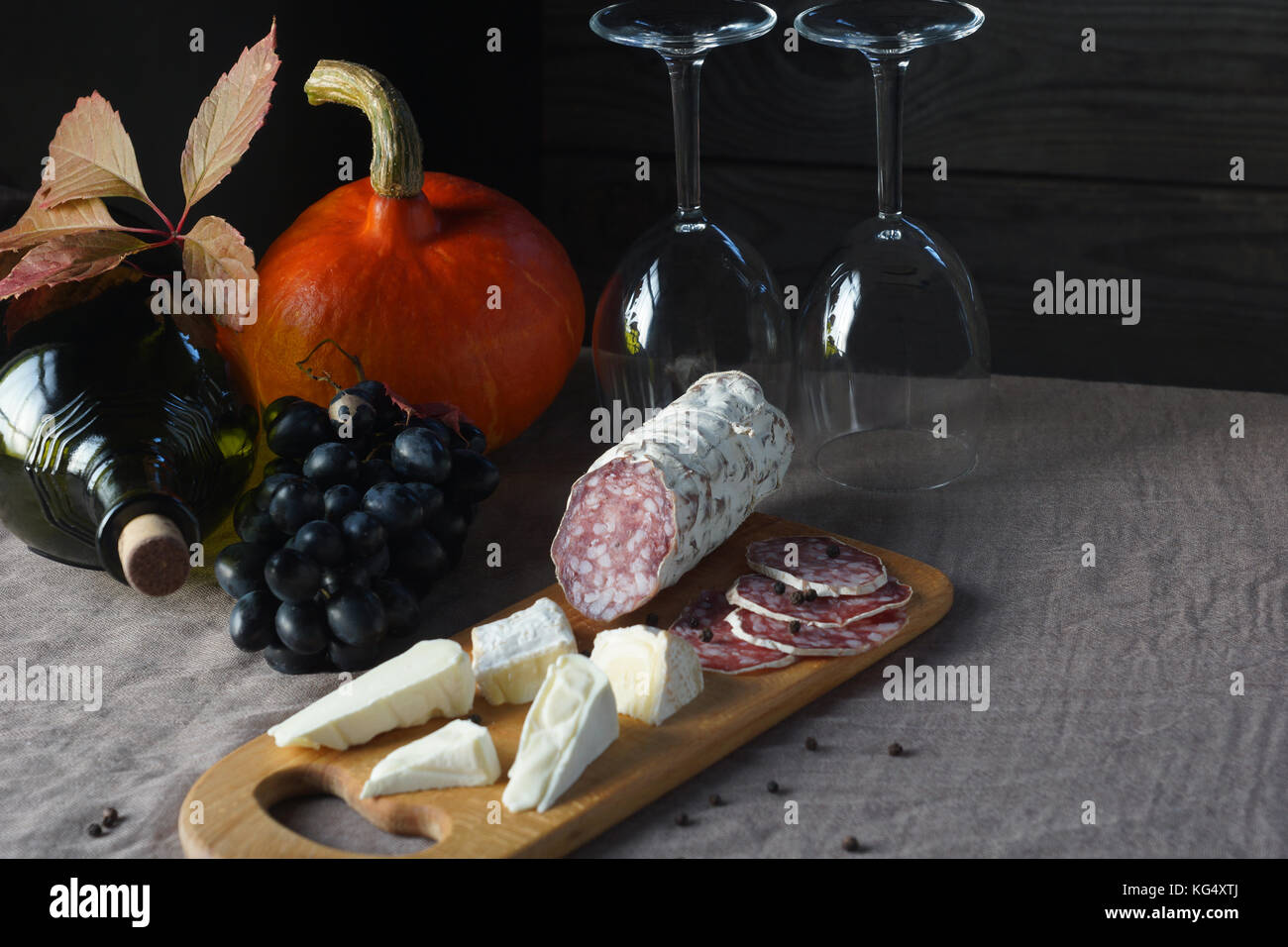 Bodegón de uvas, calabaza, botellas, vasos, quesos y embutidos en la mesa. Foto de stock