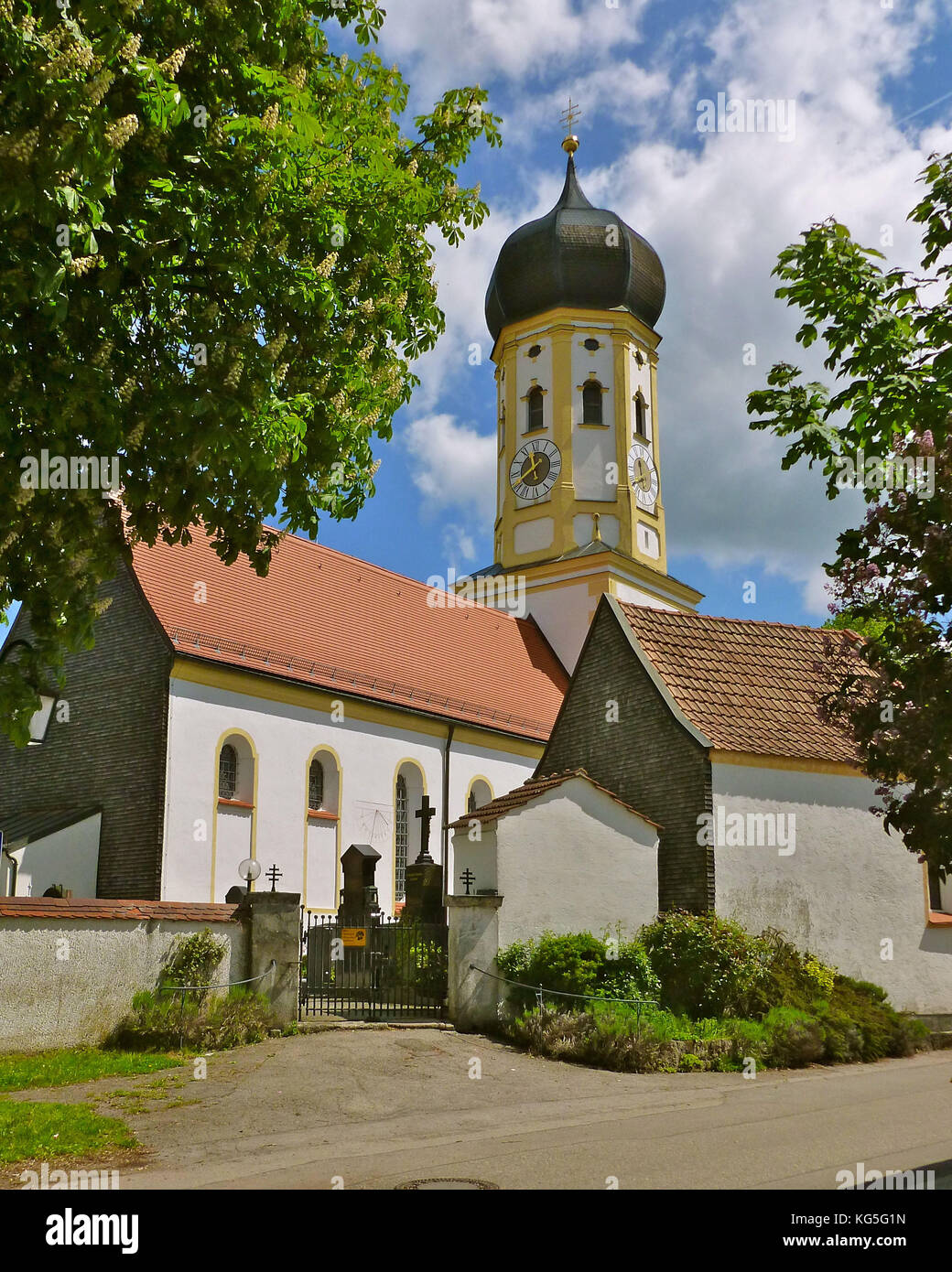 Alemania, Baviera, Aying, iglesia del pueblo, cementerio, aguja bulbosa, castaño floreciente, cielo blanco / azul Foto de stock