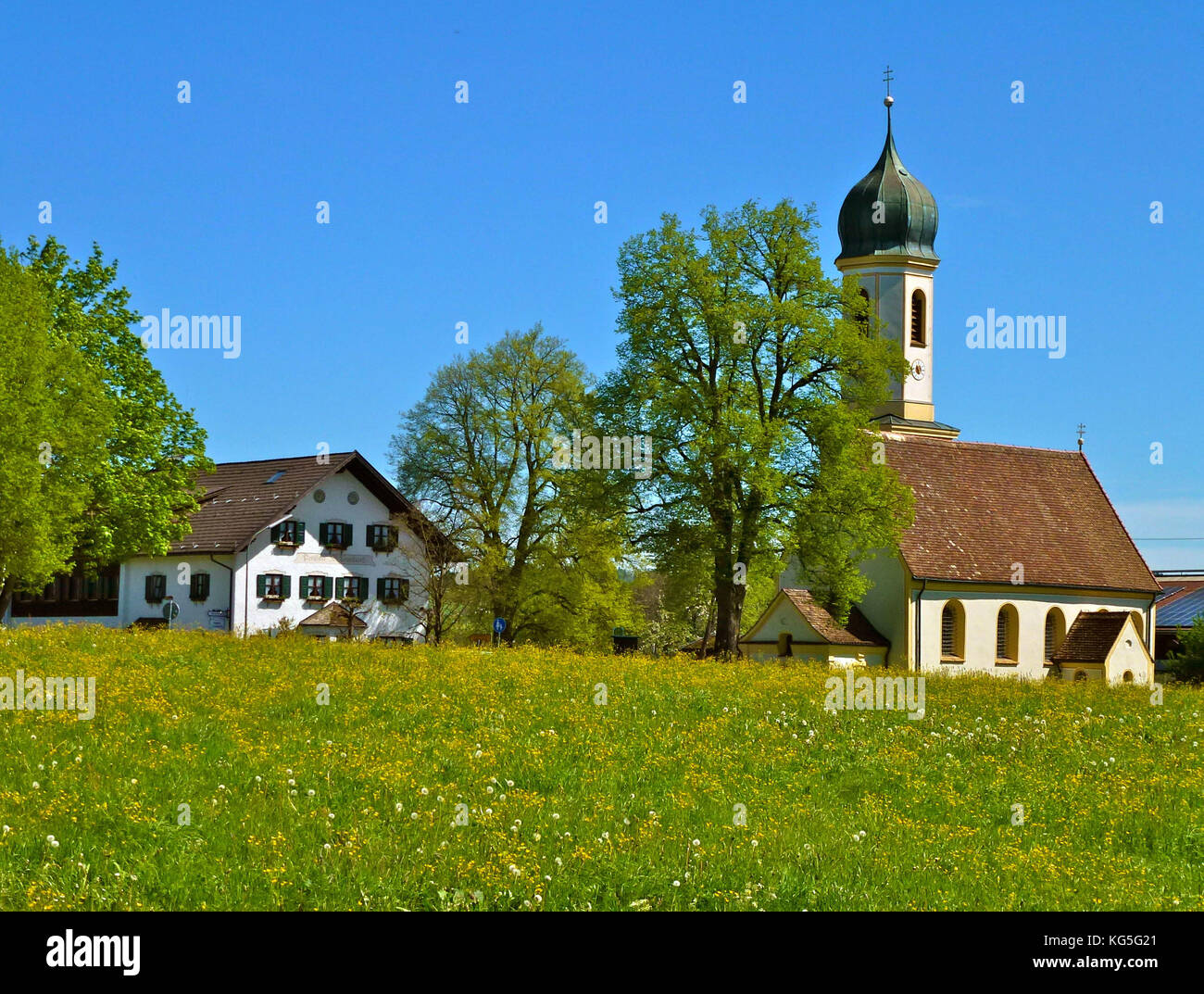 Alemania, Baviera, Froschhausen am Riegsee (lago), St. Leonhard iglesia, Pension San Leonhard (casa de huéspedes), pradera, árboles, cielo azul, la primavera Foto de stock