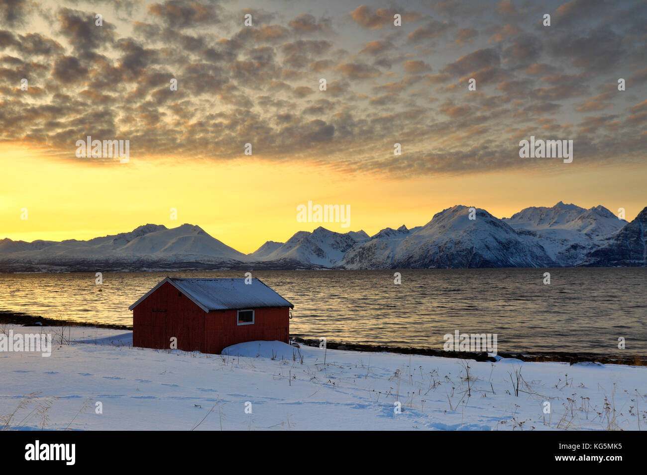 Naranja atardecer en las chozas de madera llamados Rorbu enmarcada por el mar congelado y picos nevados de los Alpes Lyngen Djupvik Tromsø Noruega Europa Foto de stock