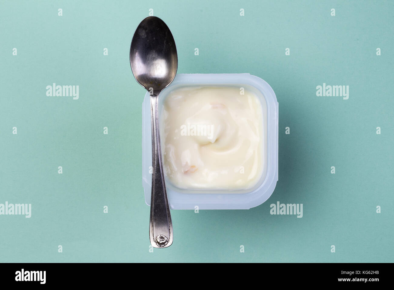 Fruta saludable yogur aromatizado con colorante natural en la cubeta de plástico aislado sobre fondo verde con una pequeña cuchara de plata - vista superior Foto de stock