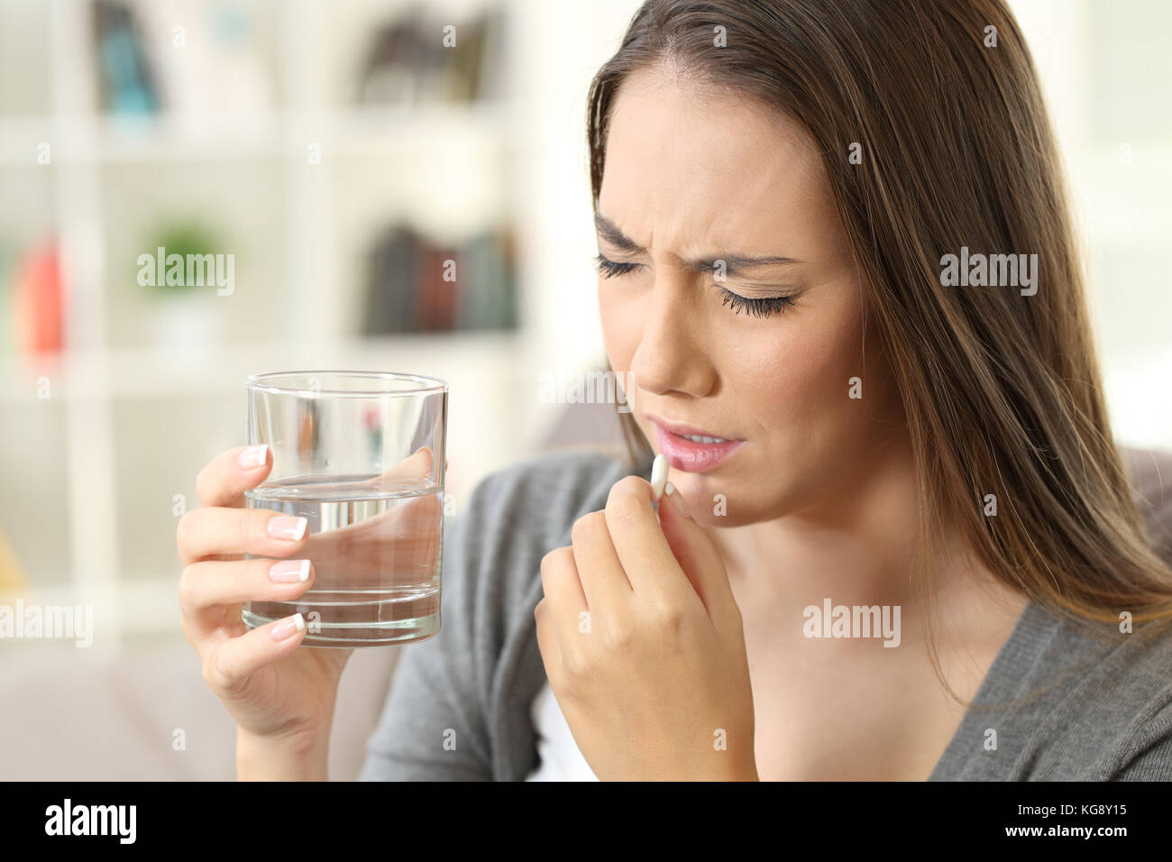 Mujer doloroso tomar una píldora sentado en un sofá en el salón en un interior de una casa Foto de stock