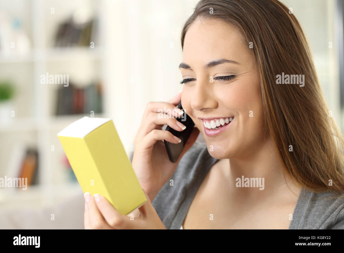 Mujer alegre y pedir información por teléfono sobre un producto sentado en un sofá en el salón en un interior de una casa Foto de stock