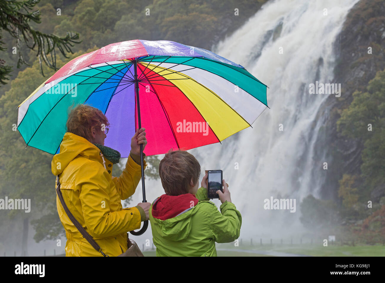 Niño tomando fotos de cascada Powerscourt, madre sosteniendo un paraguas, Enniskerry Wicklow, Irlanda, Co. Foto de stock