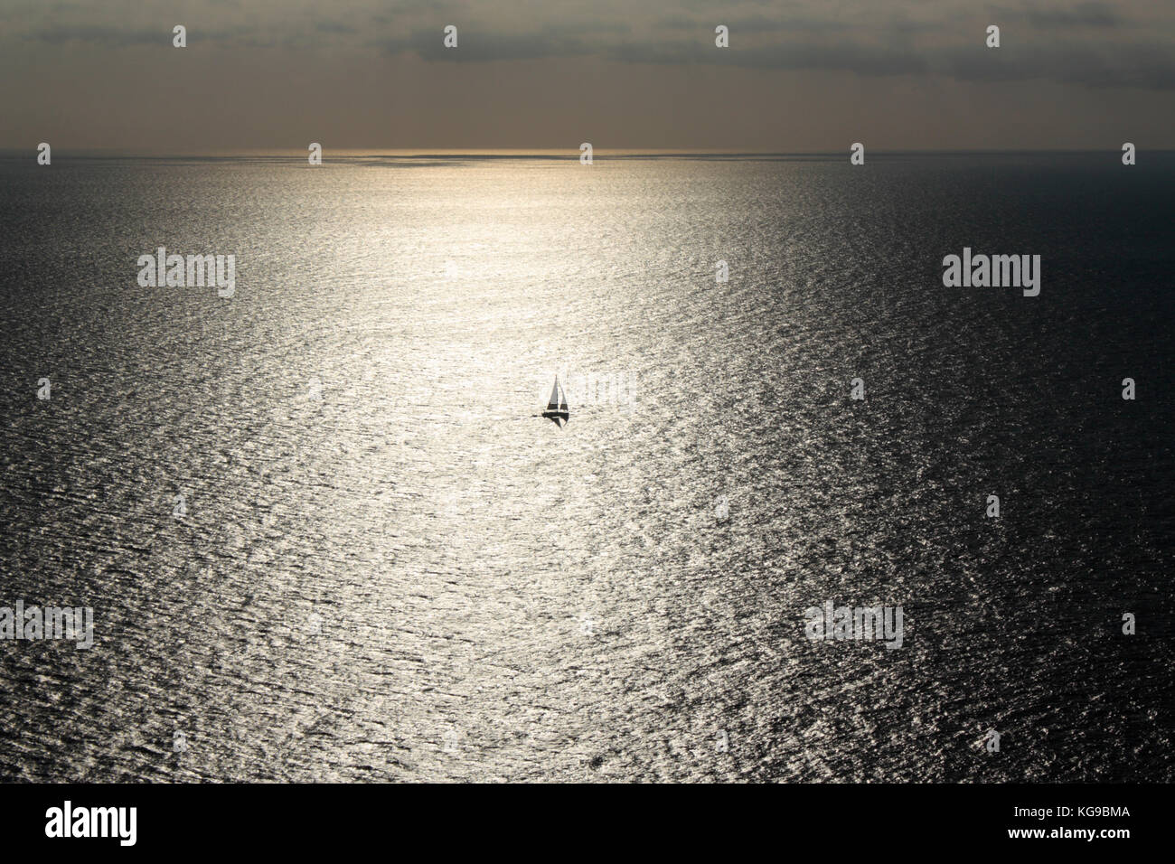 Velero o yate solitario atrapado en el sol refleja en una amplia extensión de mar Foto de stock