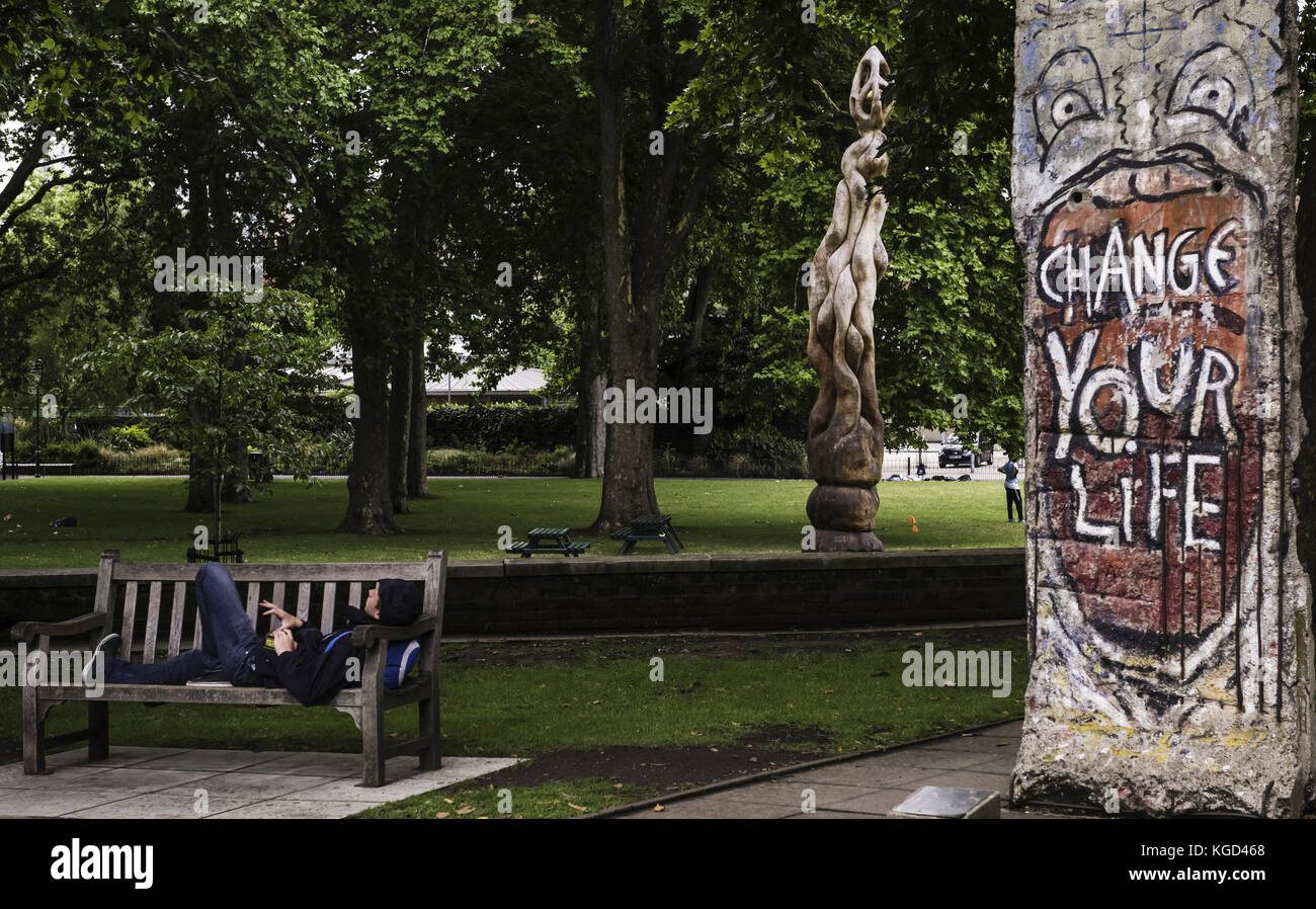 Un hombre joven se relaja en un banco mientras graffiti detrás de él dice que cambiará su vida. Foto de stock