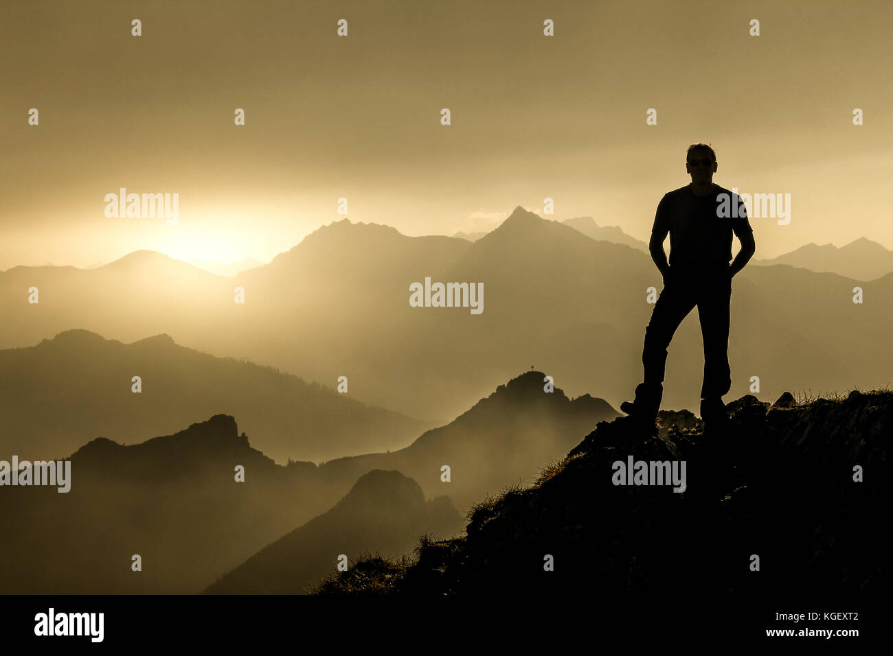 Hombre de pie en la cumbre disfrutando del amanecer y la espectacular cordillera capas siluetas. Foto de stock