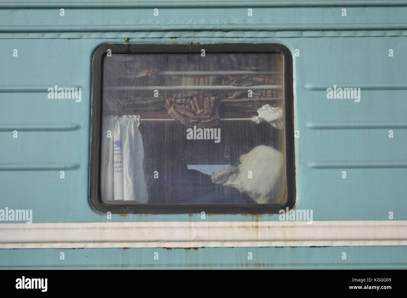 Ventana de un tren ruso azul / verde desde el exterior, mantas, bolsas y cortinas visibles. Foto de stock