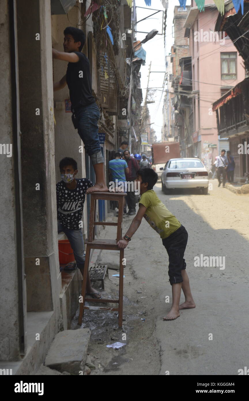 Tres niños nepaleses trabajando. Uno está en una escalera y dos están sujetando y sujetando la escalera. Escena callejera, Katmandú, Nepal. 1y después del terremoto Foto de stock