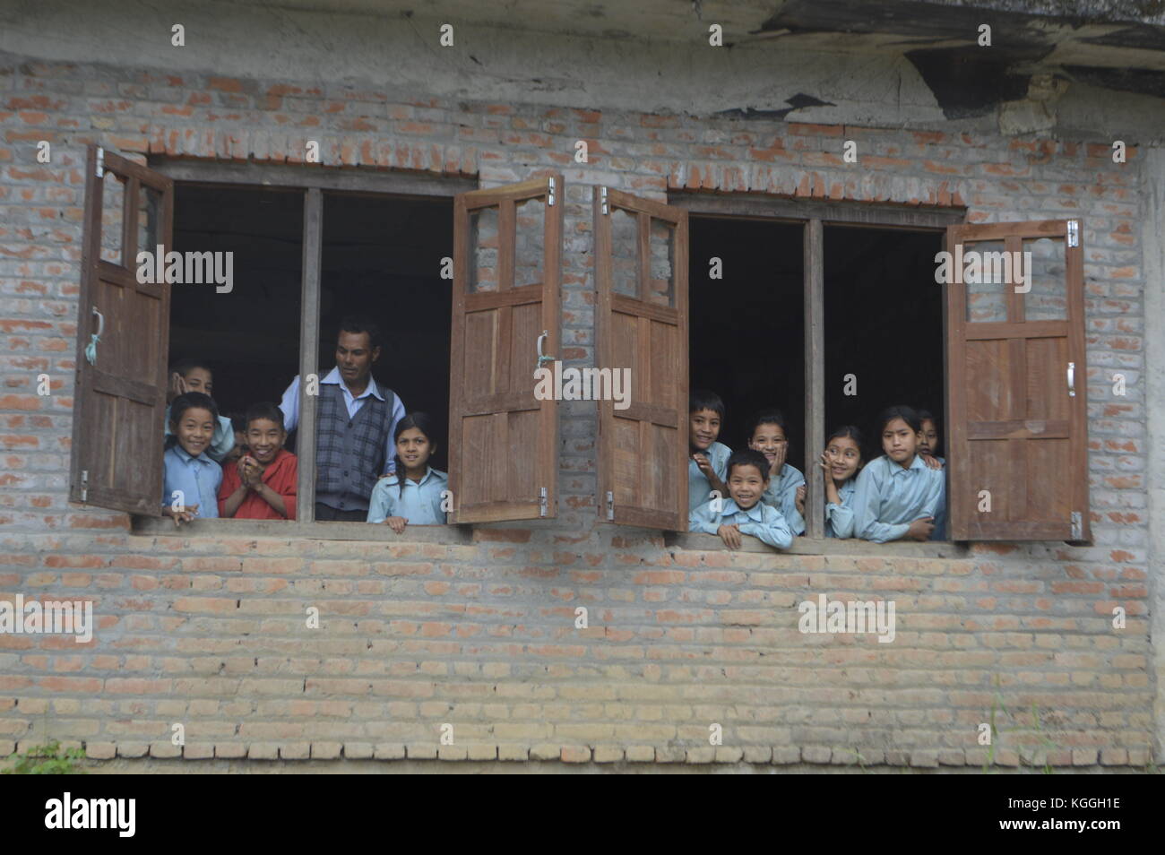 Niños nepaleses mirando por la ventana de su aula junto con su profesor curioso por quién está en su pequeño pueblo no turístico, Panauti. Foto de stock