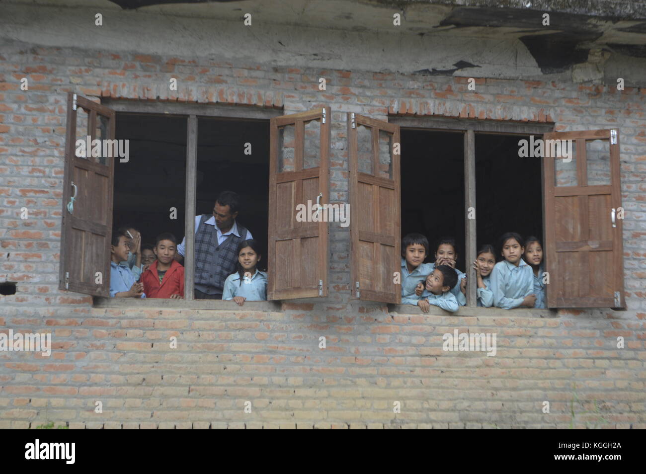 Niños nepaleses mirando por la ventana de su aula junto con su profesor curioso por quién está en su pequeño pueblo no turístico, Panauti. Foto de stock