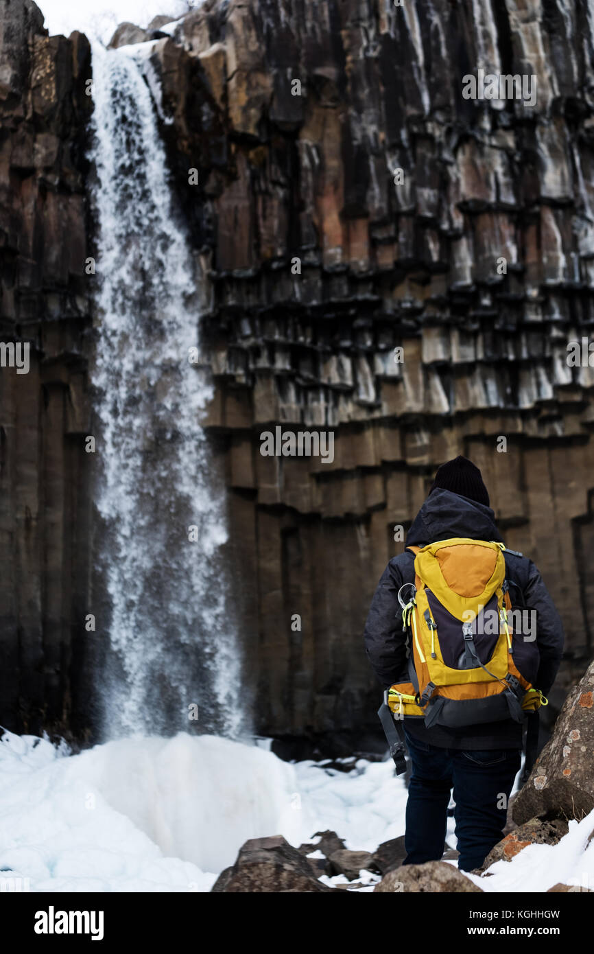 Un hombre con mochila amarilla permanecer solas svartifoss cascada en Islandia. Viajes concepto de estilo de vida Foto de stock
