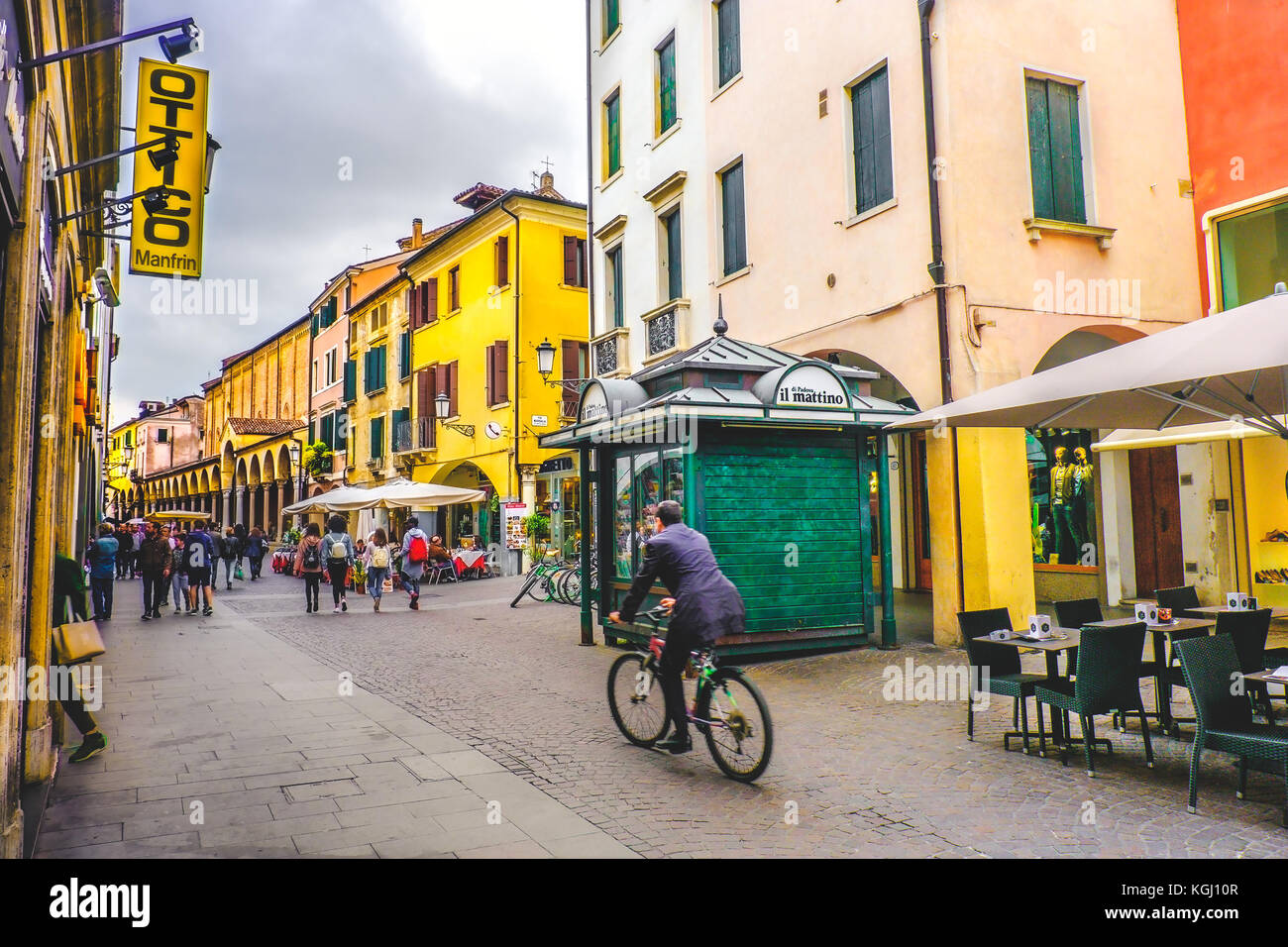 La vida cotidiana en Italia. Un hombre de negocios en bicicleta cruzando una de las vías centrales de Padua, pasando por un verde kiosco kiosco en la calle (Padova, Foto de stock