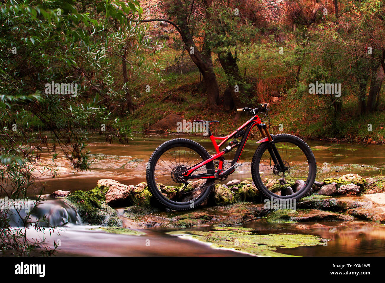Foto horizontal de una suspensión total bicicleta de montaña aisladas de pie en la corriente del río en un hermoso bosque Foto de stock