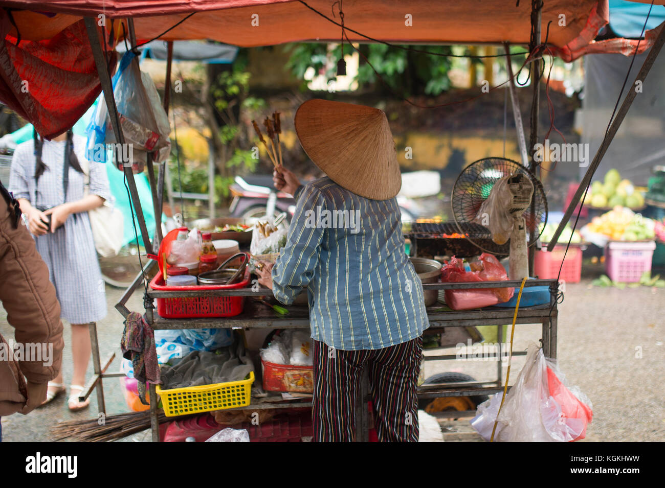 -El enfoque selectivo- mujer no identificada con los típicos sombreros cónicos vietnamitas vender hortalizas frescas y carne brochetas en un mercado callejero en Hoi An, Vietnam Foto de stock
