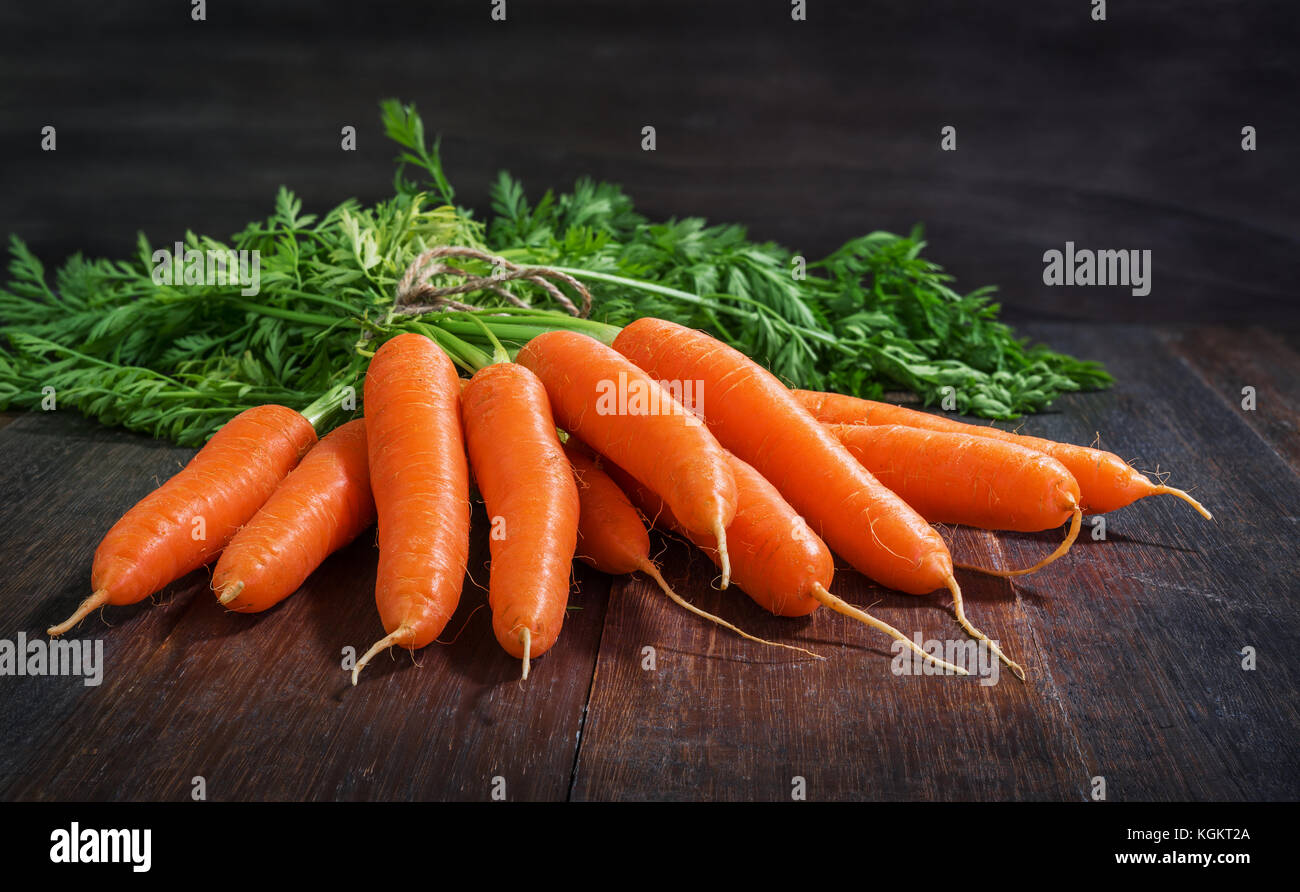 Montón de zanahorias frescas verduras con hojas verdes sobre fondo de madera rústica Foto de stock