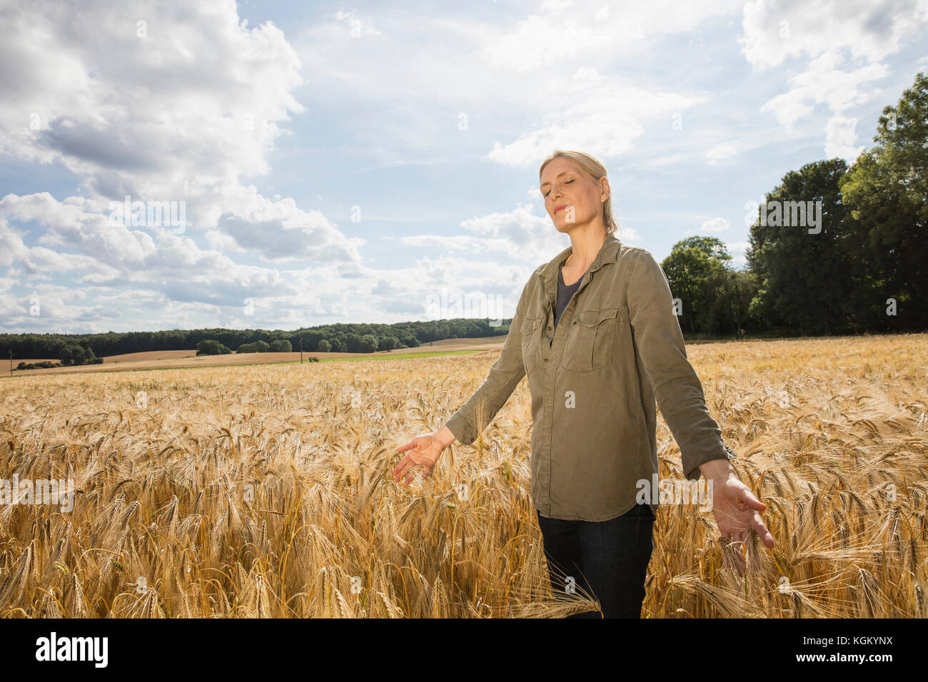 Pensativo Mujer de pie en medio de los cultivos de trigo en la granja contra el cielo en día soleado Foto de stock