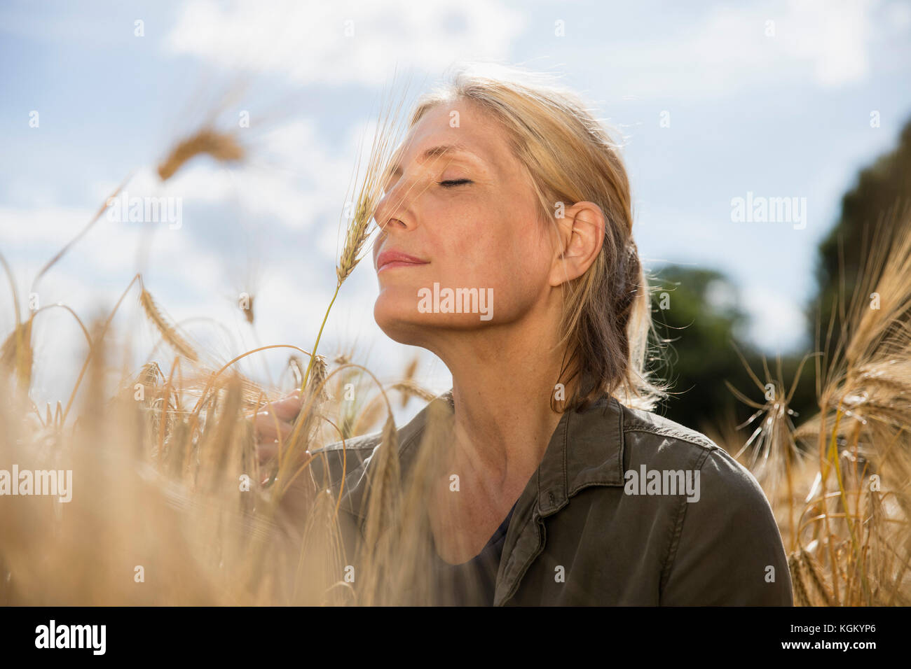 Pensativo mujer sonriente con los ojos cerrados descansando en medio de cultivos de granja en día soleado Foto de stock