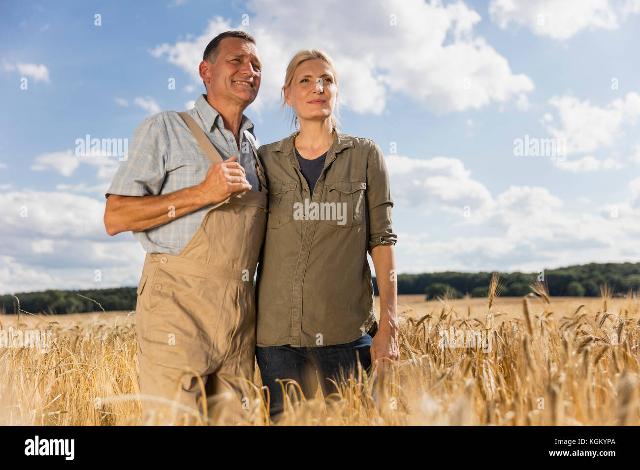 Ángulo de visión baja de la pareja de pie en medio de las cosechas en la granja contra el cielo en día soleado Foto de stock