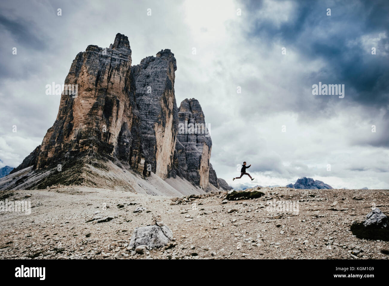Ángulo de visión baja de adolescente saltando sobre rocas en Alpes contra el cielo nublado, Tirol del Sur, Italia Foto de stock