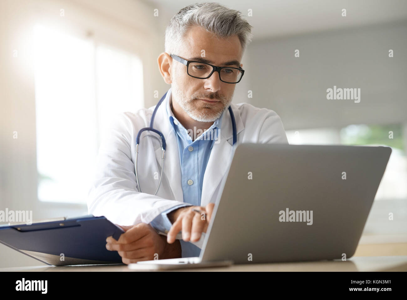 Doctor en la oficina trabajando con archivo de paciente Foto de stock