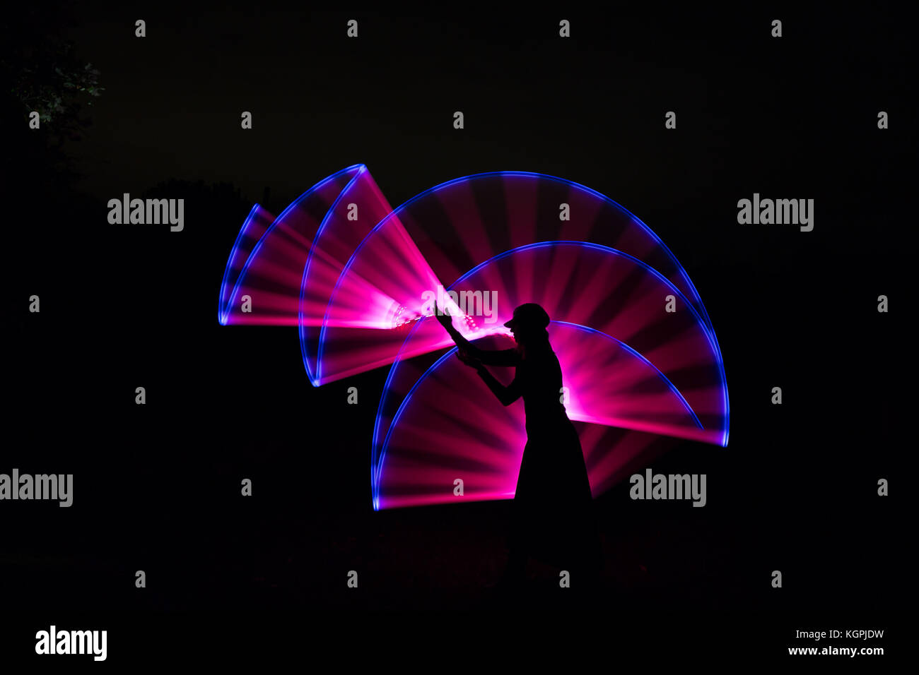 Vista lateral, silueta negra de mujeres aisladas en HAT de pie afuera en la noche, presentando los brazos en la parte delantera, con efecto de luz rosa mágica detrás. Foto de stock