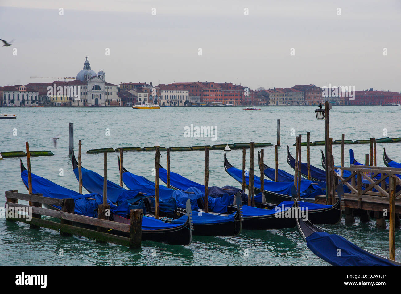 Fila de góndolas azul amarrado al muelle en Venecia, Italia, con una vista del paisaje urbano de Venecia Foto de stock