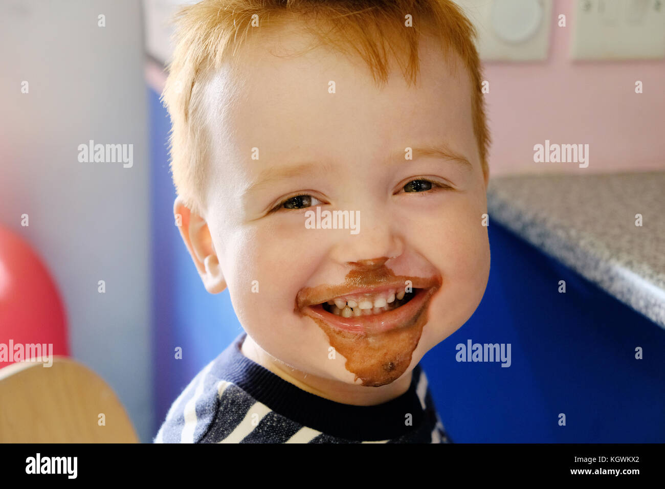 Un joven muchacho feliz, sonriendo ampliamente, su rostro cubierto de helado de chocolate habiendo comido y un helado de chocolate tratar Foto de stock