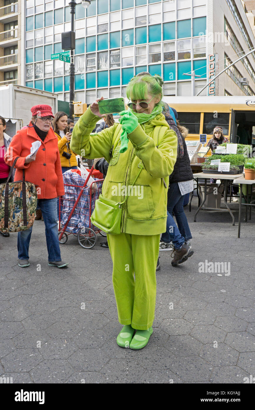 Una mujer vestida enteramente de verde lima, tomando una foto de teléfono celular. En él mercado verde de Union Square en Manhattan, Ciudad de Nueva York. Foto de stock