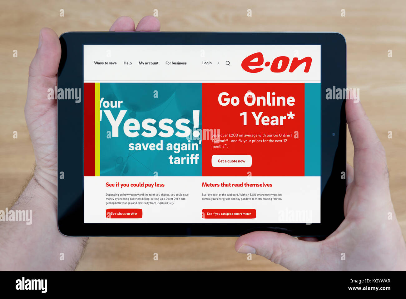Un hombre mira la página web de E.ON en su iPad dispositivo tablet, disparó contra una mesa de madera fondo superior (uso Editorial solamente) Foto de stock