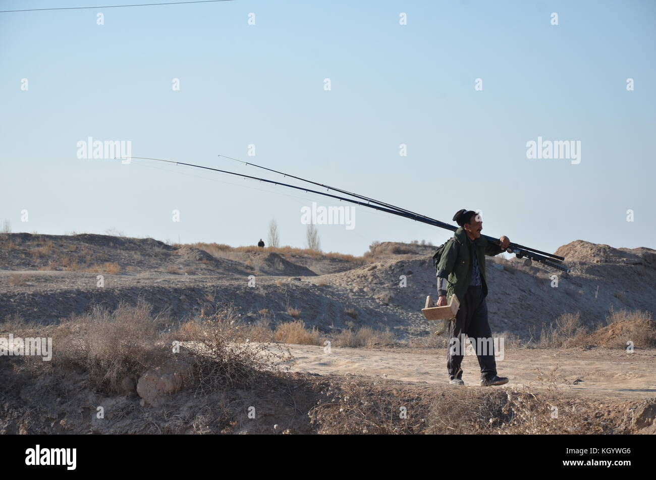 Uzbeki hombre con caña de pescar y taburete pequeño caminar en el desierto en Uzbekistán. Foto de stock