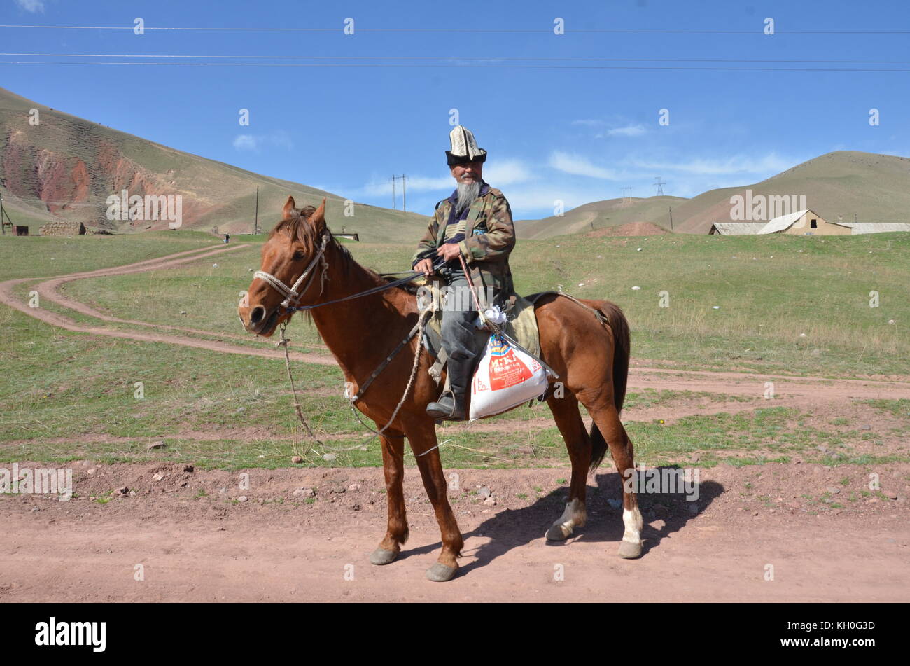 Un hombre kirguise, vistiendo un tradicional sombrero kalpak, a caballo, en Kirguistán, en Asia central. Foto de stock