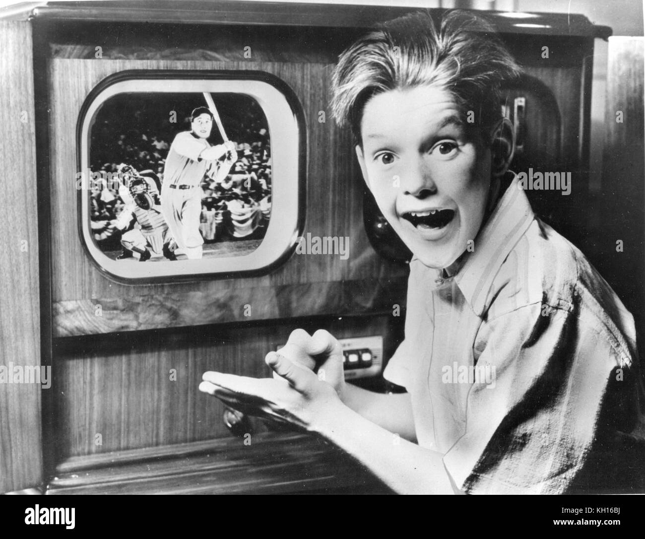 Un muchacho reacciona con emoción mientras ve un programa de televisión de un partido de béisbol en una tabla modelo establecido en su casa, 1949. Foto de stock
