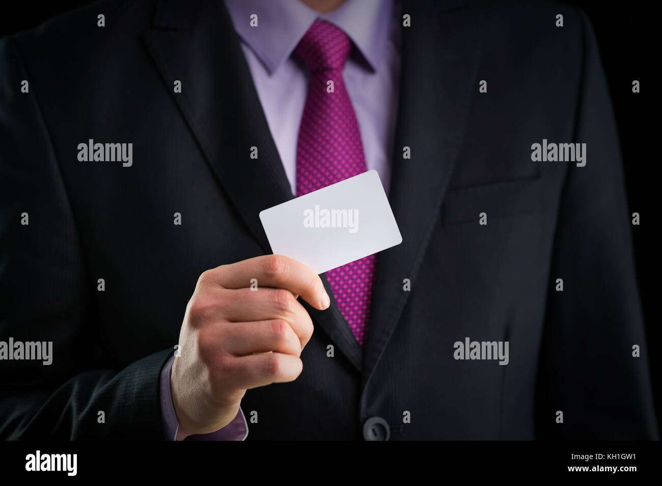 El empresario en un elegante traje y con una corbata, muestra tarjeta con copia espacio, Foto de estudio Foto de stock