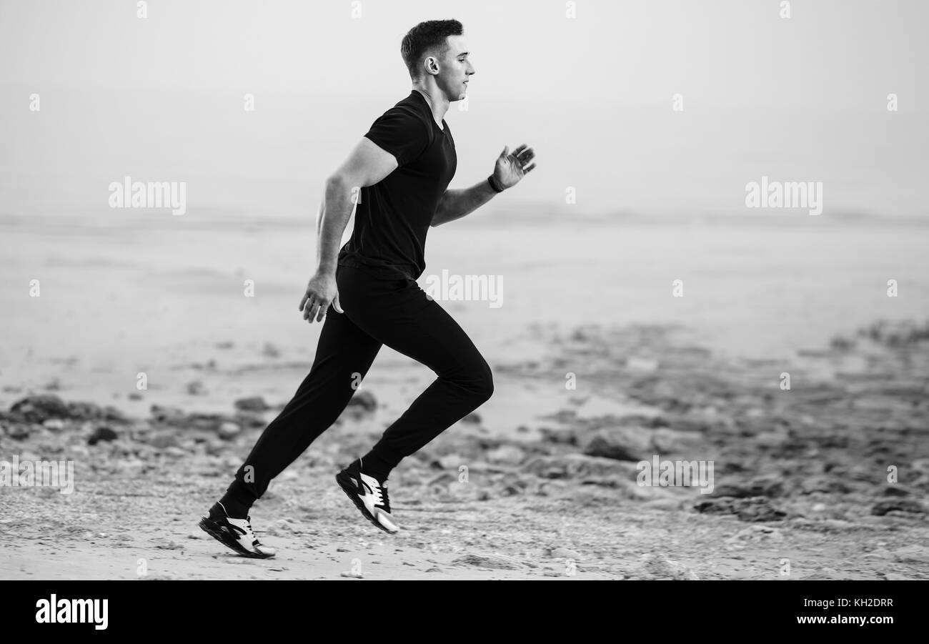 Athletic hombre corriendo por la rocosa costa junto al mar. Foto de stock