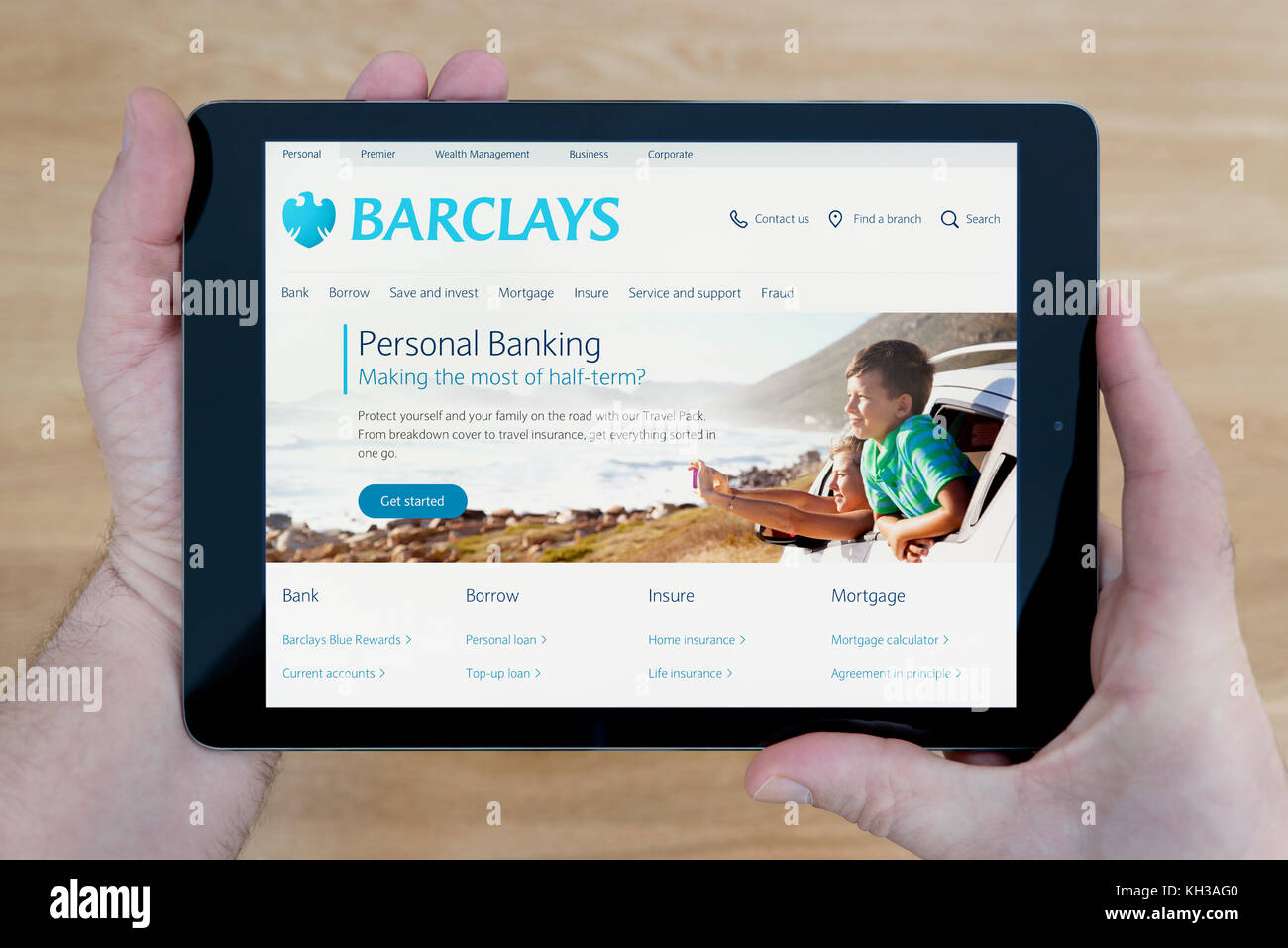 Un hombre se ve en el sitio web del banco Barclays en su iPad dispositivo tablet, disparó contra una mesa de madera fondo superior (uso Editorial solamente) Foto de stock