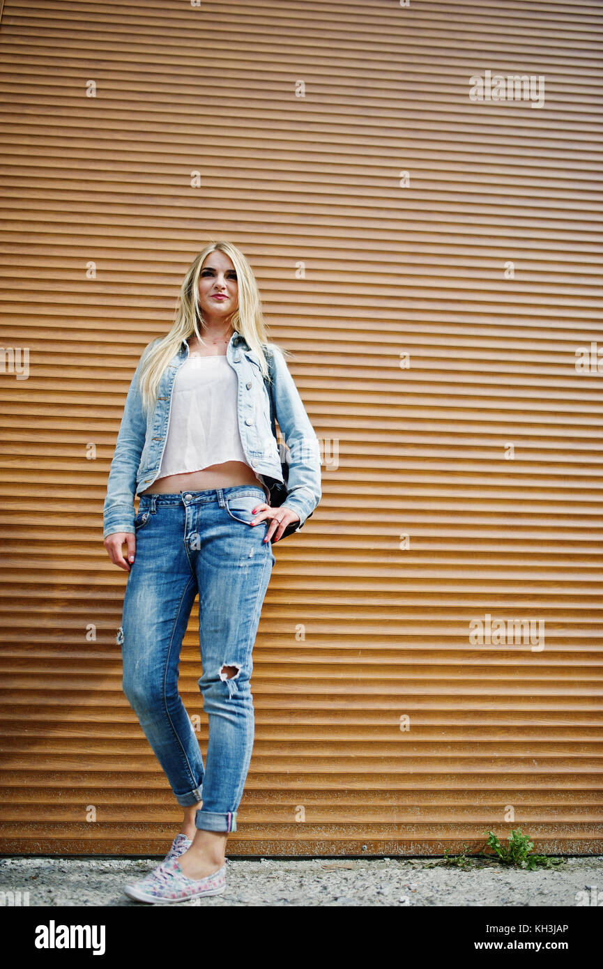 Chica rubia desgaste en los pantalones vaqueros chaqueta con naranja planteada contra el obturador Fotografía de stock - Alamy