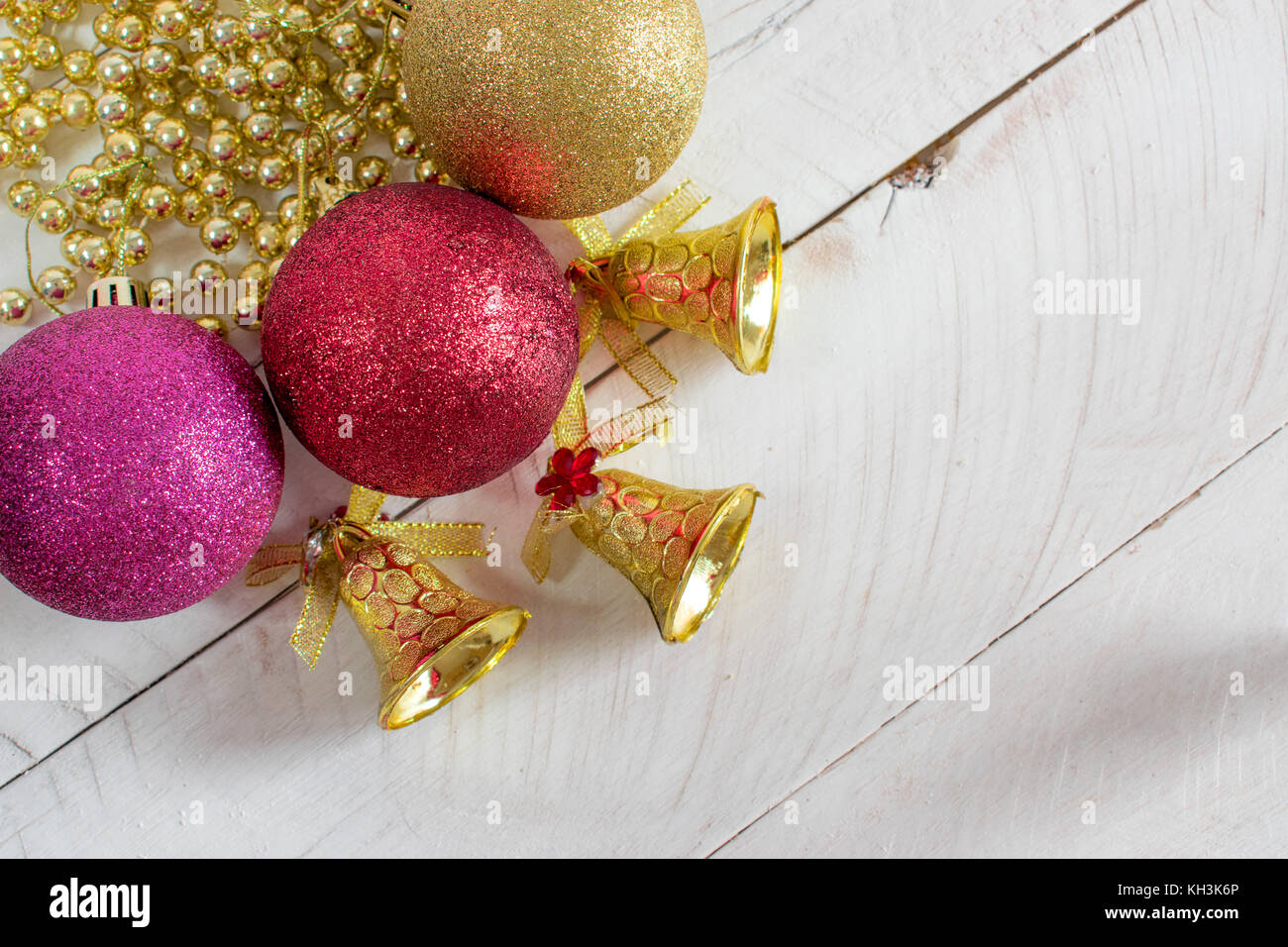 Decoración de Navidad, cadenas, campanas y coloridas bolas reflectantes, encima de una superficie de madera blanca y fondo blanco. Foto de stock