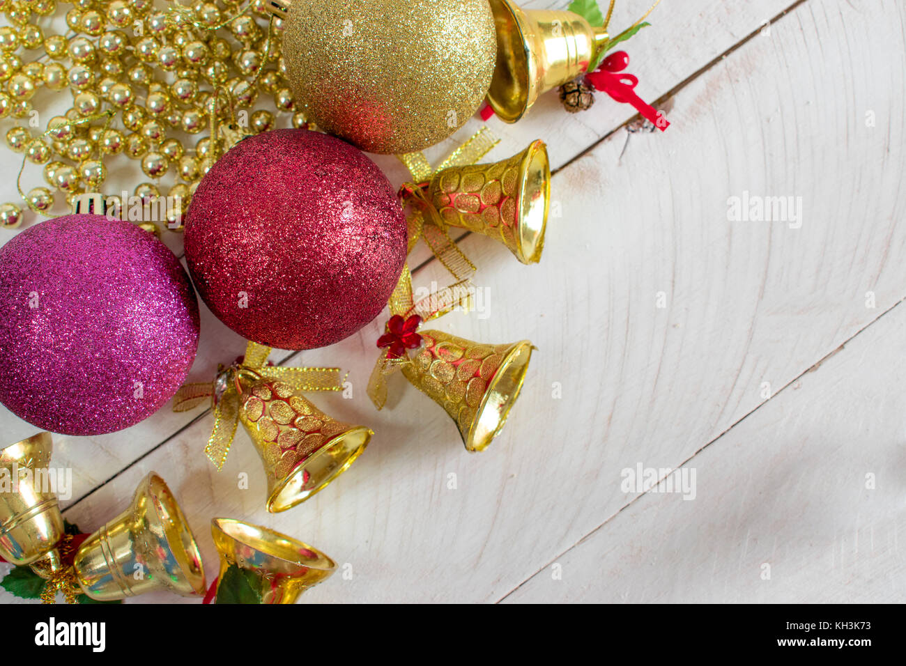 Decoración de Navidad, cadenas, campanas y coloridas bolas reflectantes, encima de una superficie de madera blanca y fondo blanco. Foto de stock
