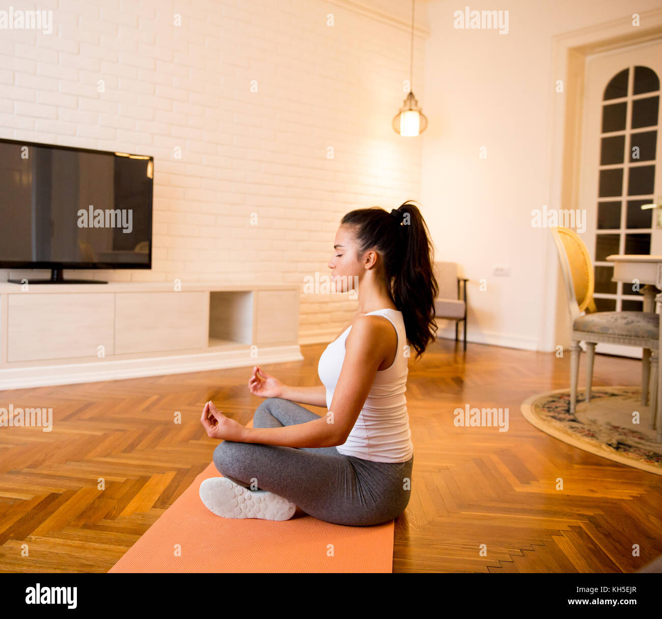 Mujer joven sentada en el piso en su casa haciendo Yoga Meditación Foto de stock