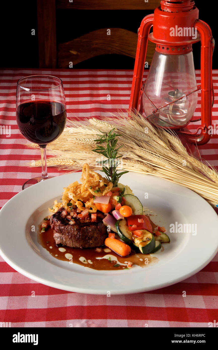 Toda la cena de bistec americano se sirve con vino tinto sobre tela de vichy rojo. Foto de stock